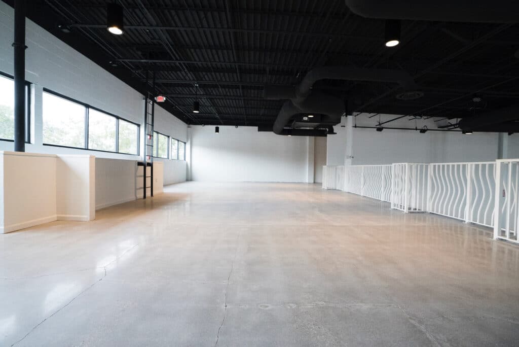 empty modern event space with white walls, large windows, black ceiling, and wood floors